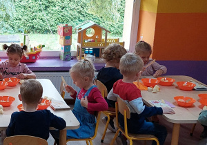 Dzieci siedzą przy stolikach i przygotowują sałatkę warzywną